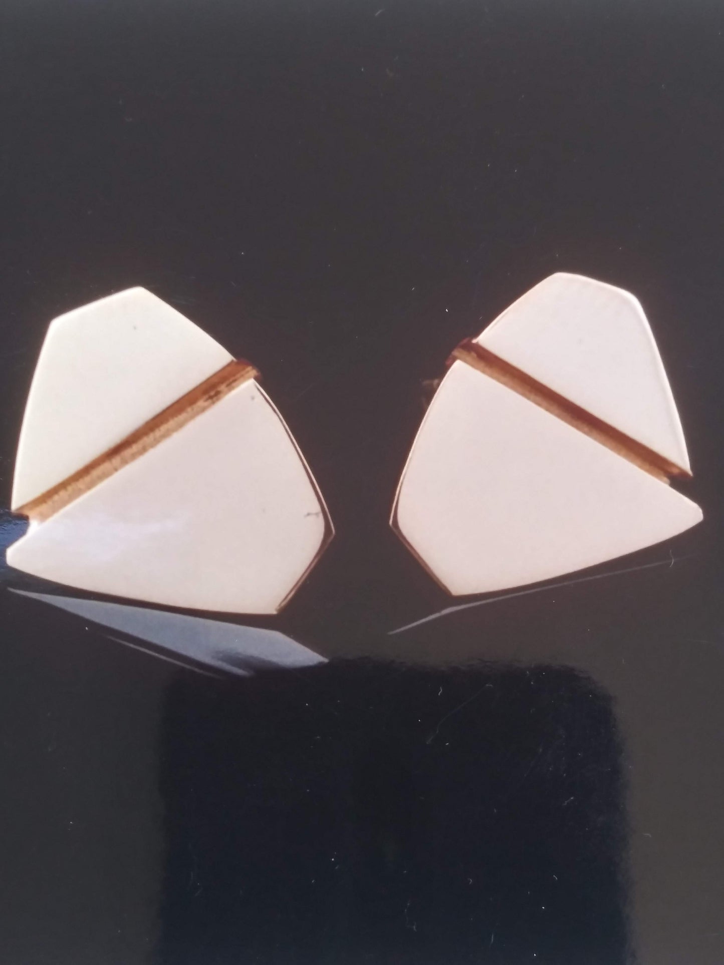 A pair of gold cufflinks with a raised gold stripe bisecting a white enamel inlay.