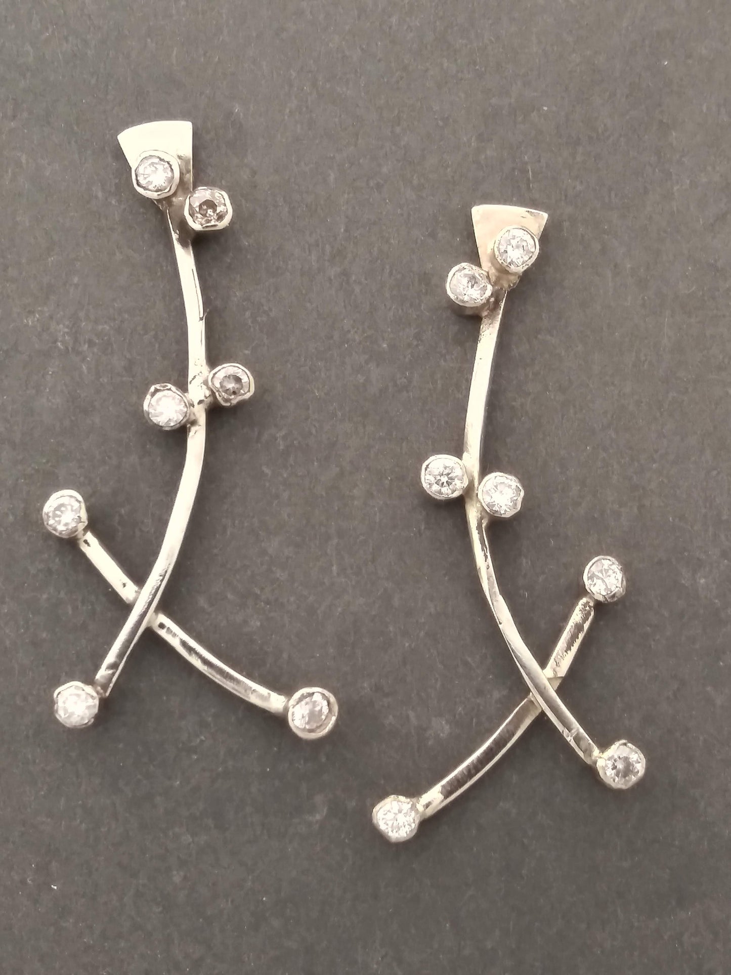 A pair of silver earrings with small diamonds set in a branch-like design that curves up the ear.