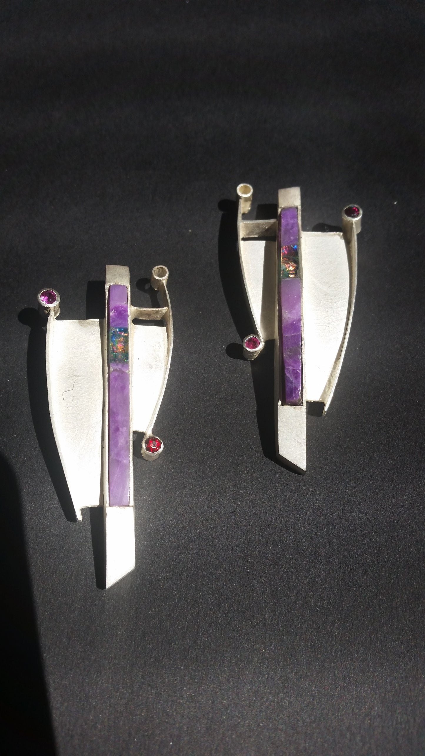Two silver brooches with purple and red gemstones, set in a modern, abstract design.