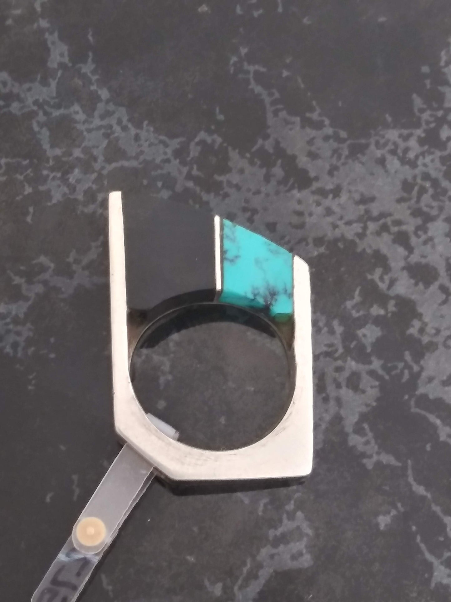 A silver ring with a wide, geometric band featuring inlays of black onyx and turquoise.