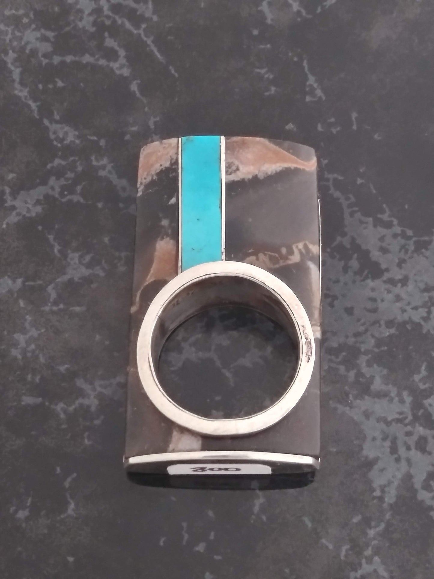 A rectangular ring with a large flat top. The top is made of brown and beige marbled stone with a vertical turquoise inlay. The ring band is silver.