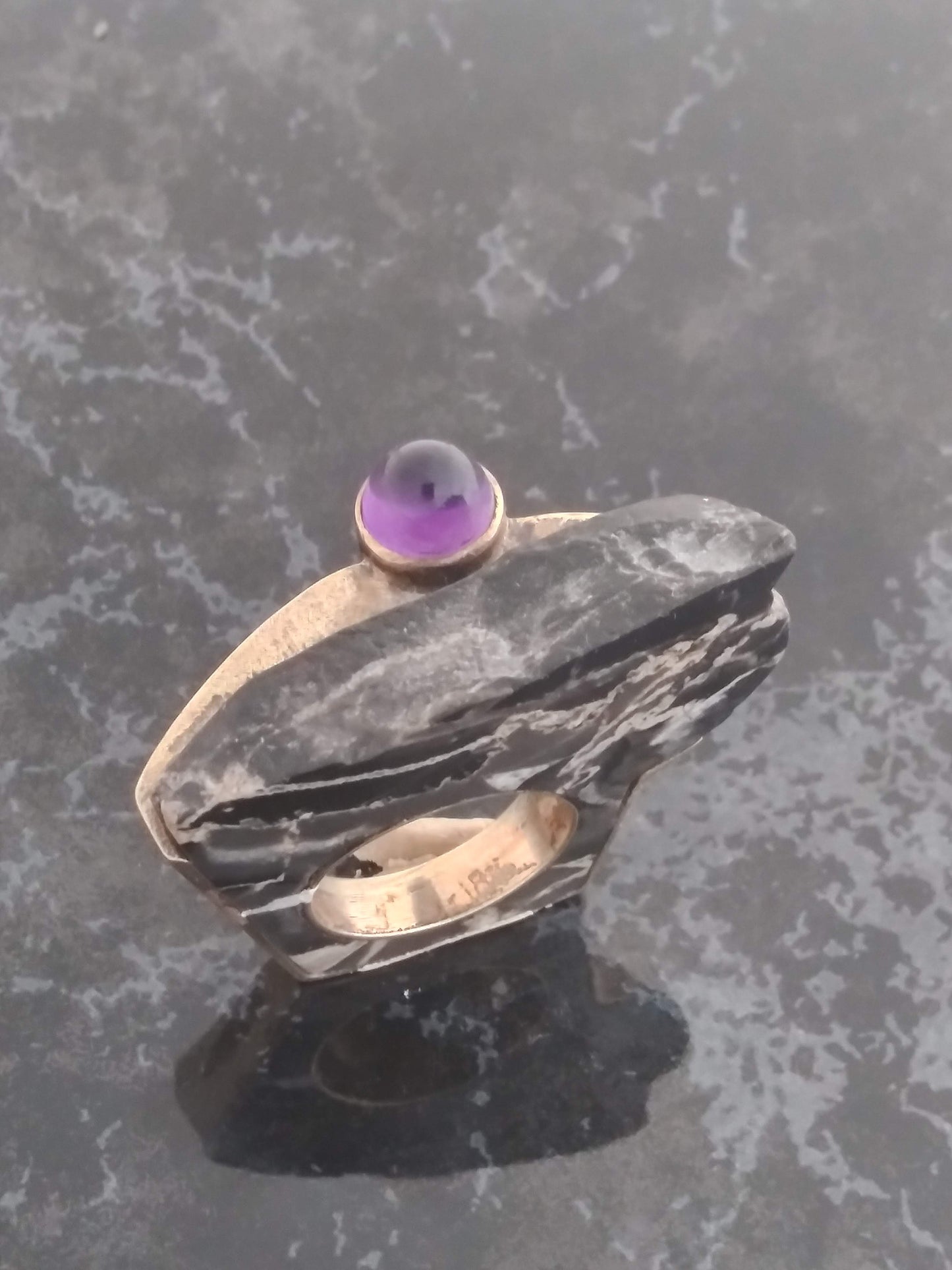 A gold and black marble ring with a round purple amethyst gemstone on top.