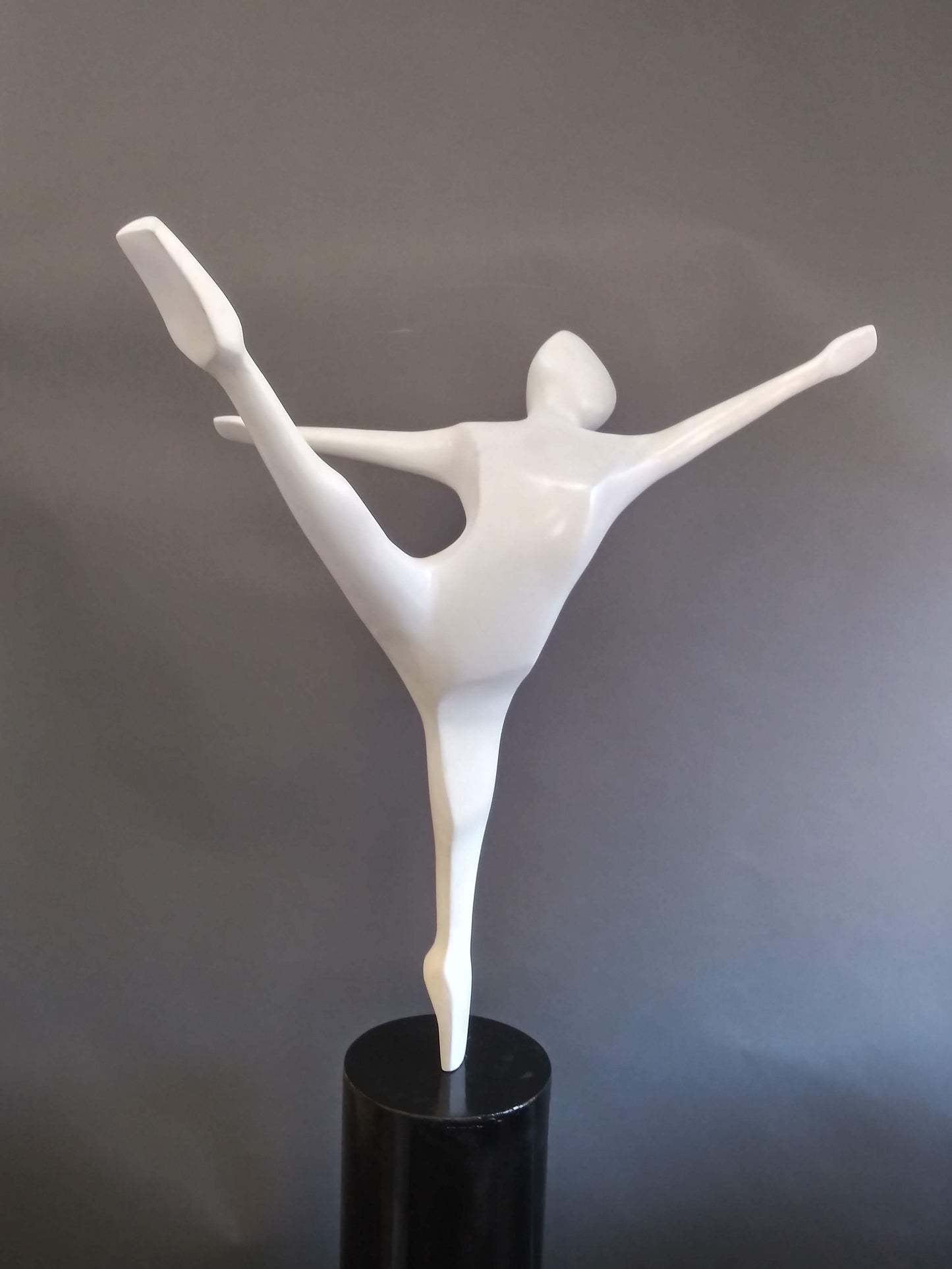 A white sculpture of a ballerina balancing on one pointe shoe with the other leg extended high behind her and both arms outstretched.