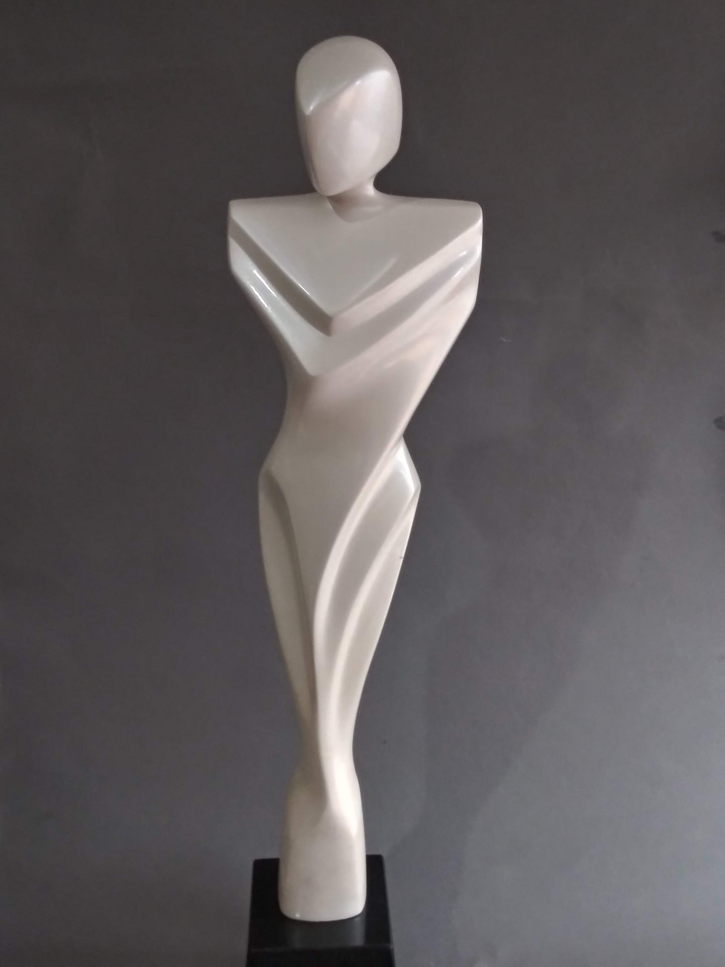 A white, abstract sculpture of a human figure with sharp, geometric angles and curves, mounted on a black base.