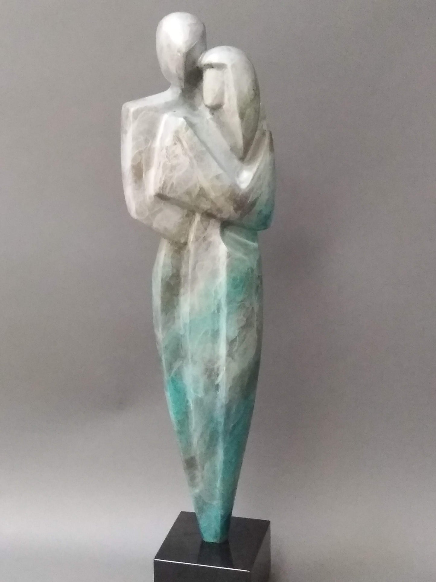 A bronze sculpture by Reno Carollo titled 'Tenderness'. It depicts two abstract figures embracing, with the taller figure holding the other in their arms.